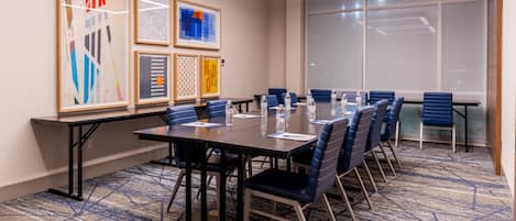 A conference room with a long table, blue chairs, and framed artwork on the walls.