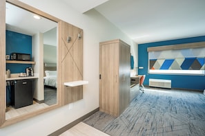 A modern hotel room with a large mirror, a wooden wardrobe, a small kitchenette, and a bed with white bedding. - Holiday Inn Express & Suites Charlottesville by IHG (Charlottesville)