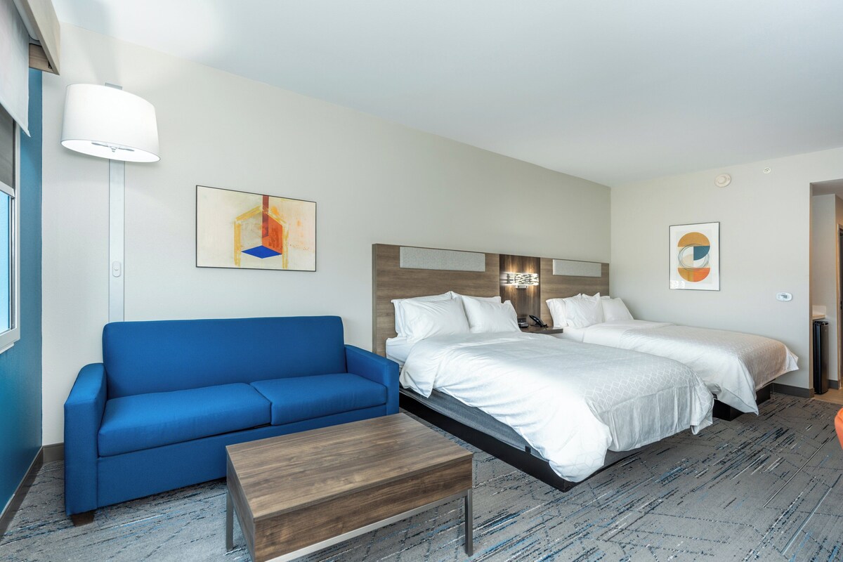 Une chambre d’hôtel avec un canapé bleu, une table basse en bois, un grand lit avec une literie blanche et deux tables de chevet.