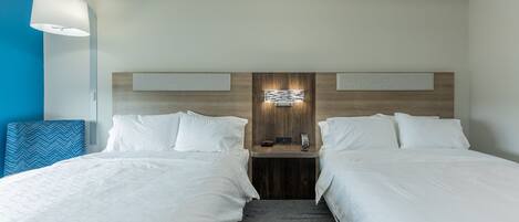 A hotel room with two beds, a wooden headboard, a nightstand with a phone and a clock, and a blue accent wall.