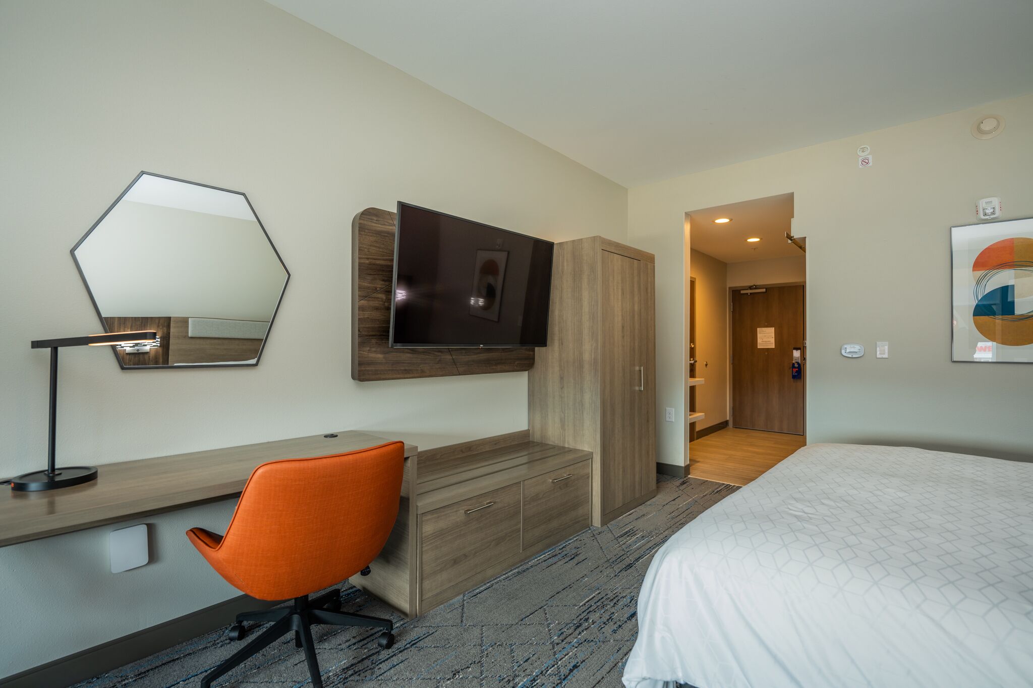 A hotel room with a bed, a desk with a chair, a TV mounted on the wall, and a wardrobe.