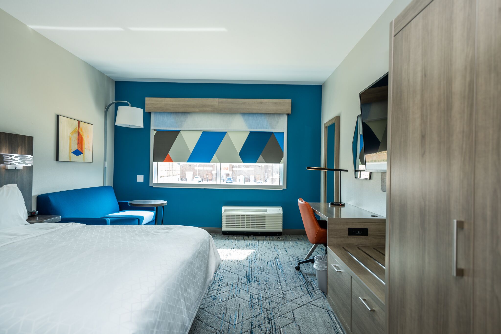 A hotel room with a bed, a desk, a chair, a TV, and a window with a city view.