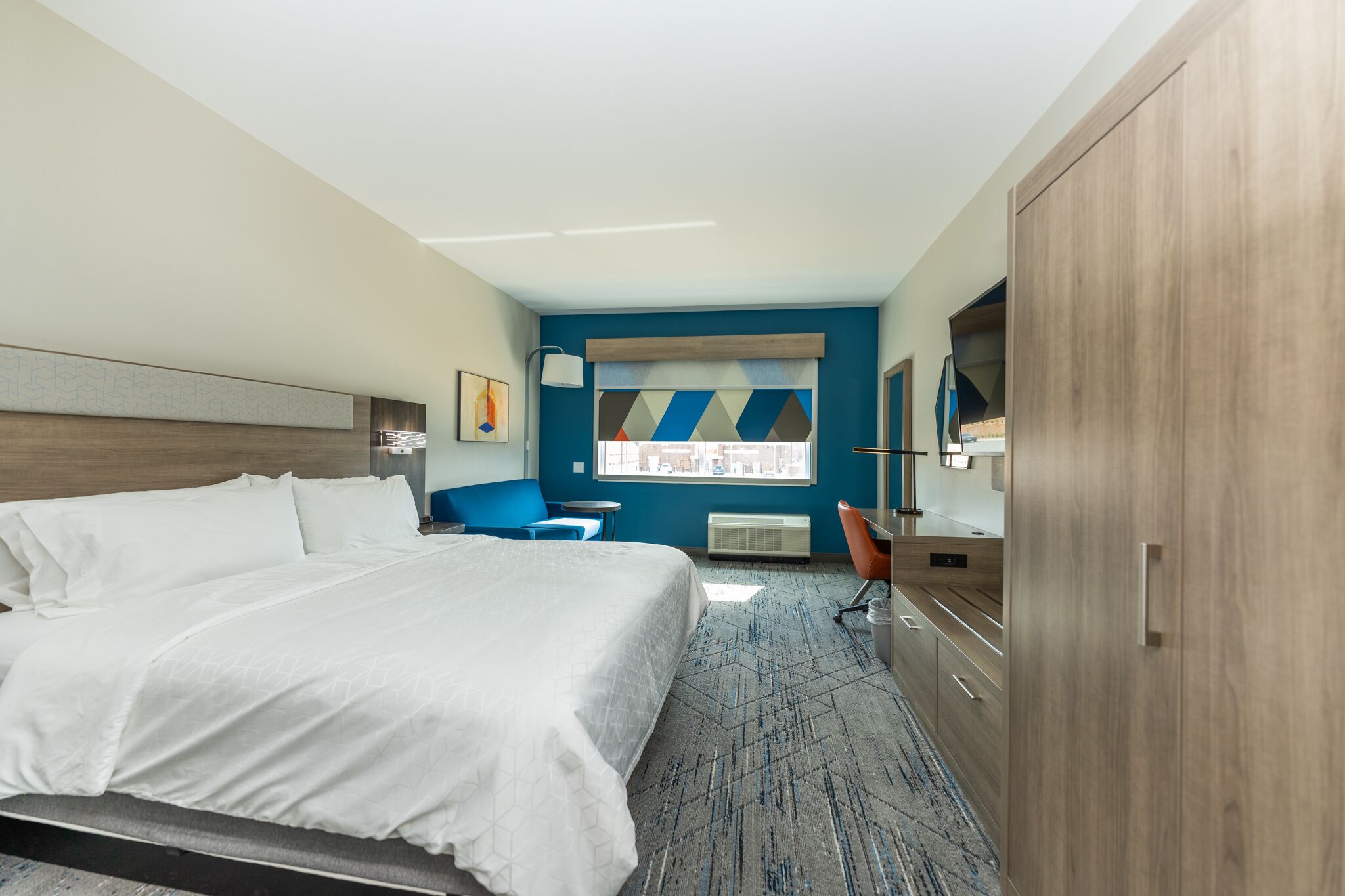 Une chambre d’hôtel avec un grand lit, un bureau, une chaise et une armoire.