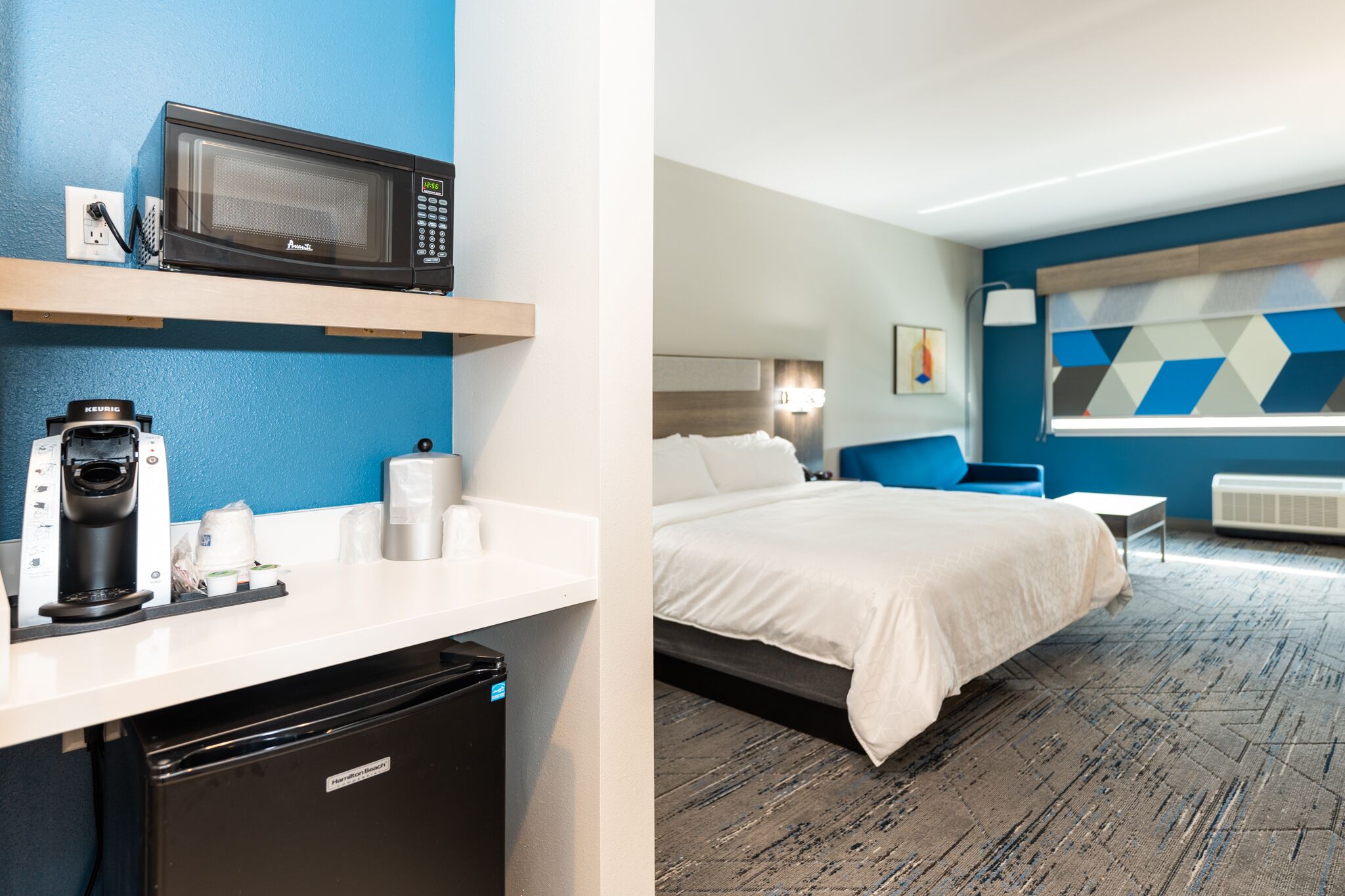 Ein Hotelzimmer mit Küchenzeile, einem Bett, einer blauen Akzentwand und einem modernen Design.