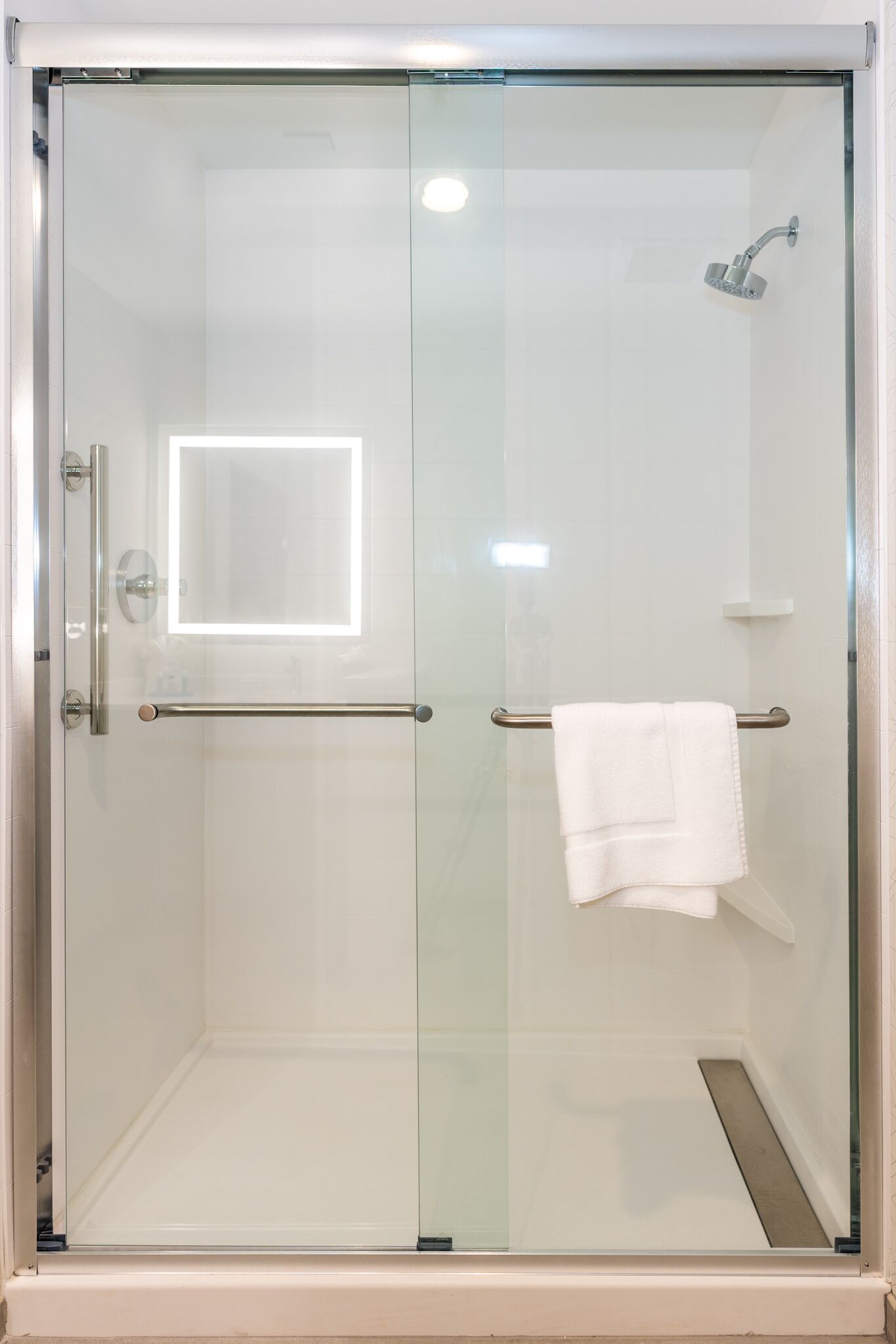 A glass-enclosed shower with a handheld showerhead, a towel rack, and a small shelf.