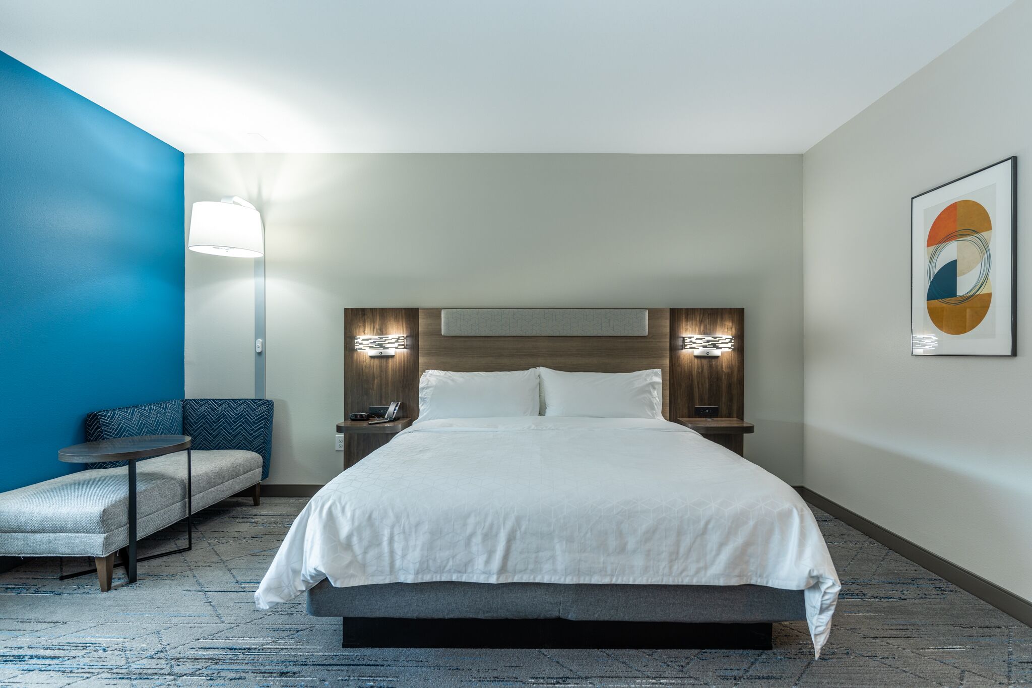 A hotel room with a large bed, a sofa, a small table, and a wall-mounted lamp.