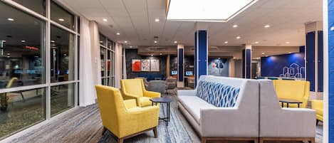 Eine moderne Lobby mit Sitzbereichen, großen Fenstern und einer blauen Akzentwand.