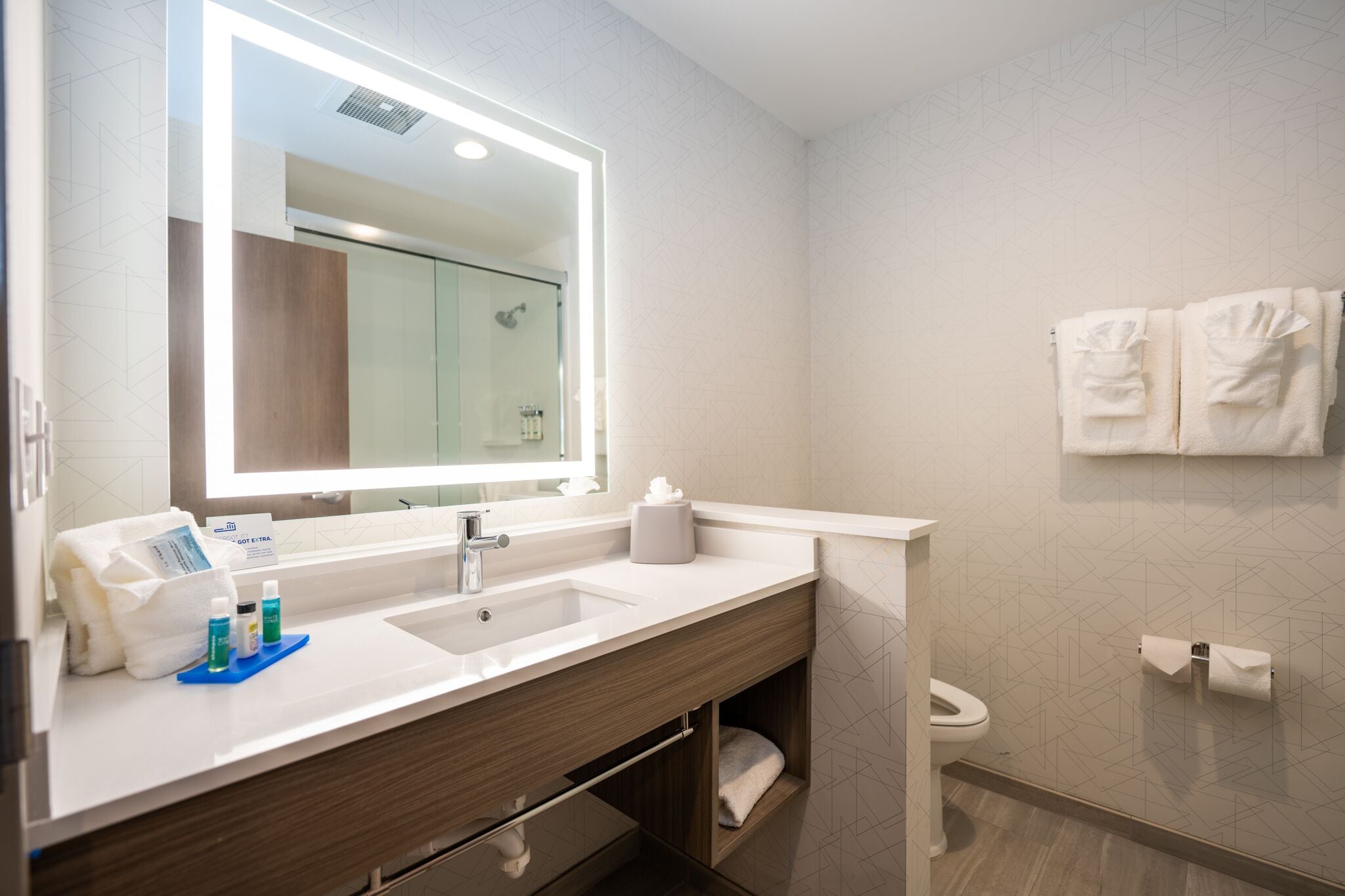 A modern bathroom with a large mirror, dual sinks, and a shower.