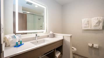 A modern bathroom with a large mirror, dual sinks, and a shower.