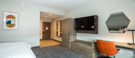 Habitación de hotel con una cama, un escritorio con una silla, un televisor y un espejo.