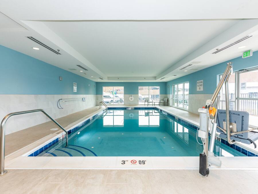 An indoor swimming pool with clear water, a lifeguard chair, and a sign indicating a depth of 3 feet and a width of 9 feet.