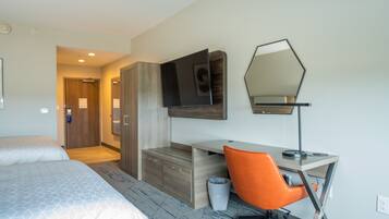 A hotel room with two beds, a desk with a computer, a chair, a trash bin, and a mirror.