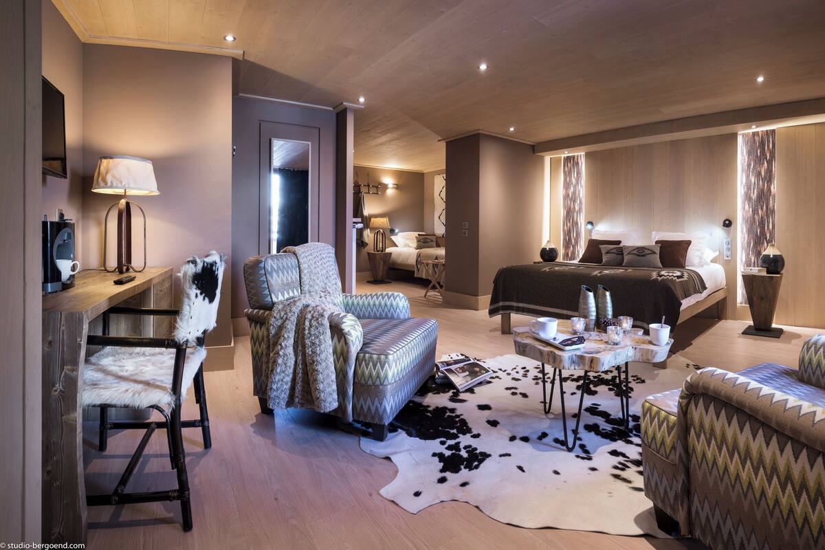 A modern hotel room with a large bed, a desk with a computer, a chair, and a cowhide rug.