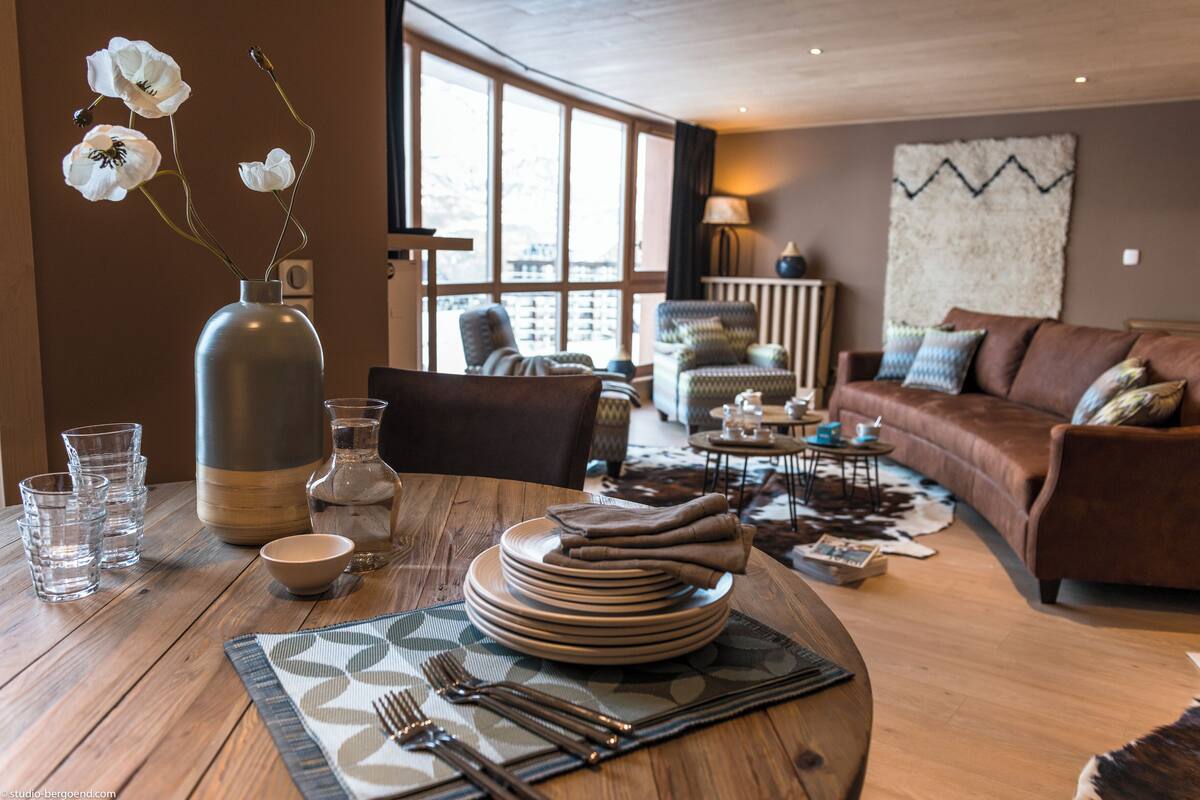 A dining area with a wooden table set for four, including plates, bowls, and cutlery. There is a vase with white flowers on the table.
