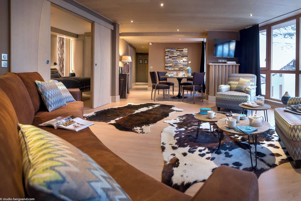 A modern living room with a large window, a cowhide rug, and a dining area with a table and chairs.