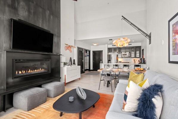 Un salon moderne avec une cheminée, des canapés gris et un coin repas à l’arrière-plan.