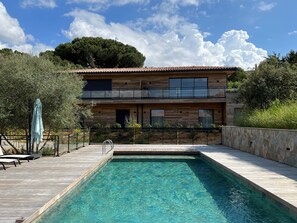 Ein modernes, zweistöckiges Haus mit Schwimmbad, Holzterrasse und Steinmauer.