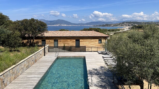 A wooden building with a tiled roof, a swimming pool, and a view of the sea and mountains.