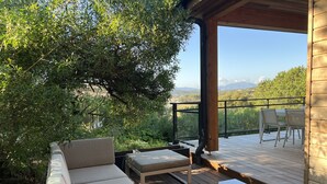 A wooden deck with a sofa, a table, and a chair, overlooking a mountainous landscape.