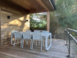 Ein überdachter Essbereich im Freien mit einer Holzterrasse und weißen Stühlen.