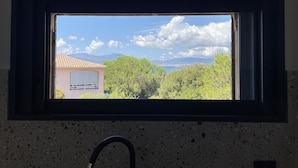 A window with a view of a building with a tiled roof, trees, and mountains in the background.