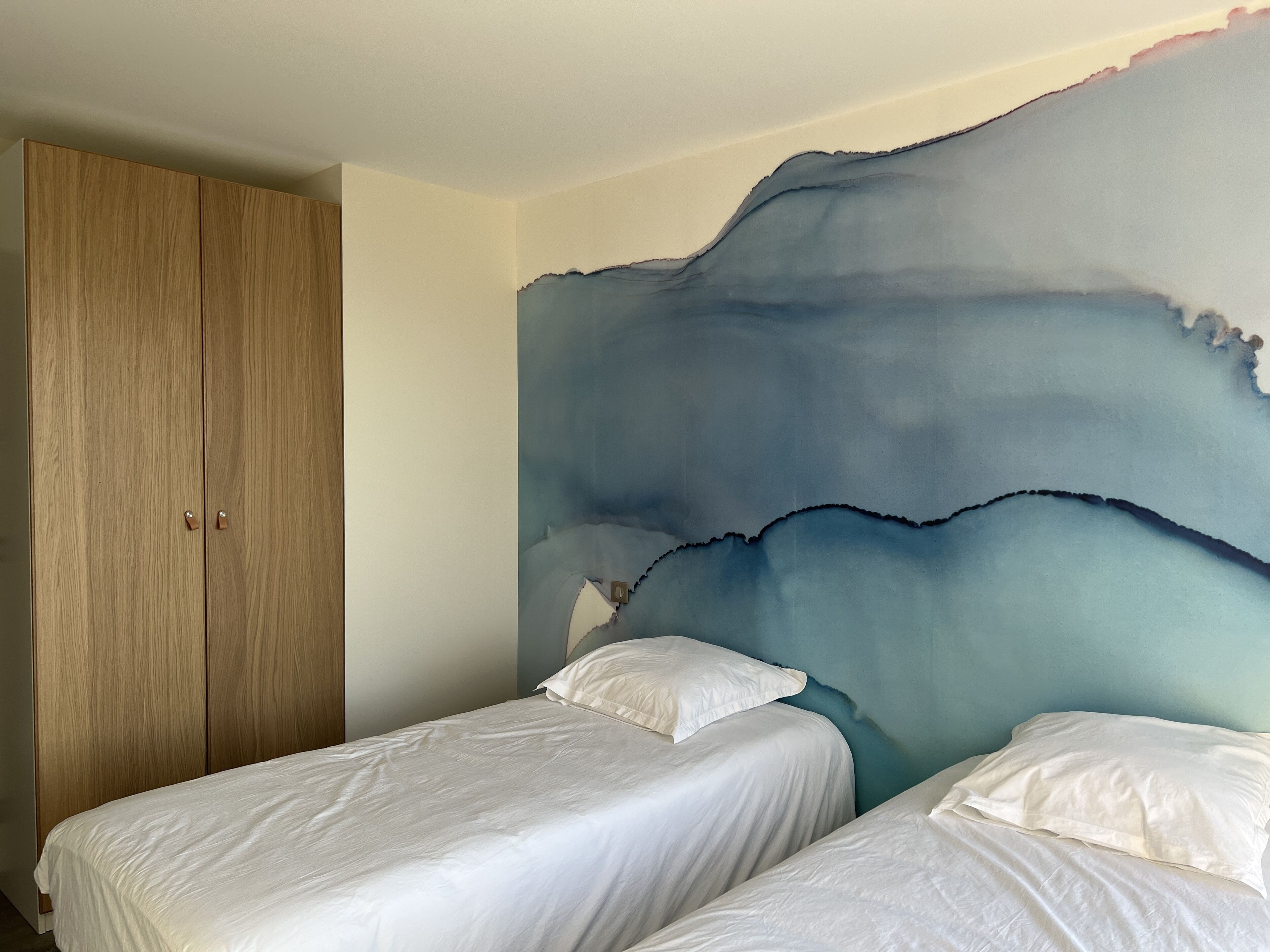 Un dormitorio con dos camas individuales, un armario de madera y un cuadro grande de estilo abstracto.