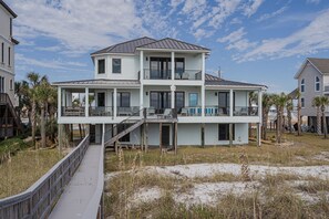 A two-story beachfront house with a covered porch and a wooden deck.