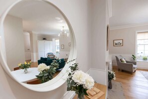 A living room with a large mirror, a teal sofa, a grey armchair, and a dining area with a white table and yellow flowers. - Beautiful Apartment in Richmond, North Yorkshire (Richmond)