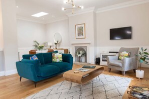 A living room with a teal sofa, a wooden coffee table, a grey armchair, and a fireplace.