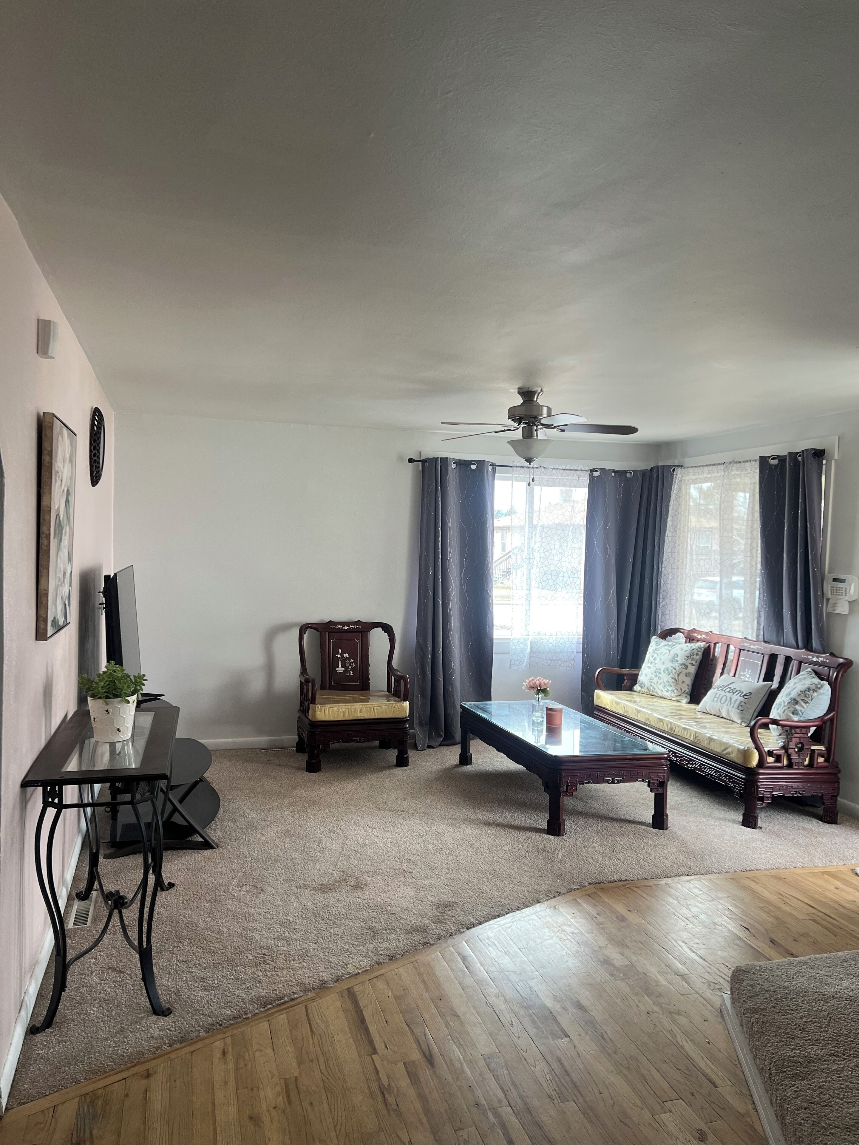 Un salon avec un plancher en bois, une table basse en verre, un canapé, un fauteuil et un ventilateur de plafond.