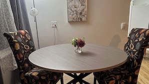 Ett runt matbord med stolar som har ett blommönster, en vas med blommor och en tavla som hänger på väggen.
