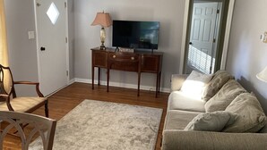 A living room with a wooden floor, a television on a stand, a lamp, a sofa, and a chair. - Buffalo Ny Carols Cape (Bowmansville)