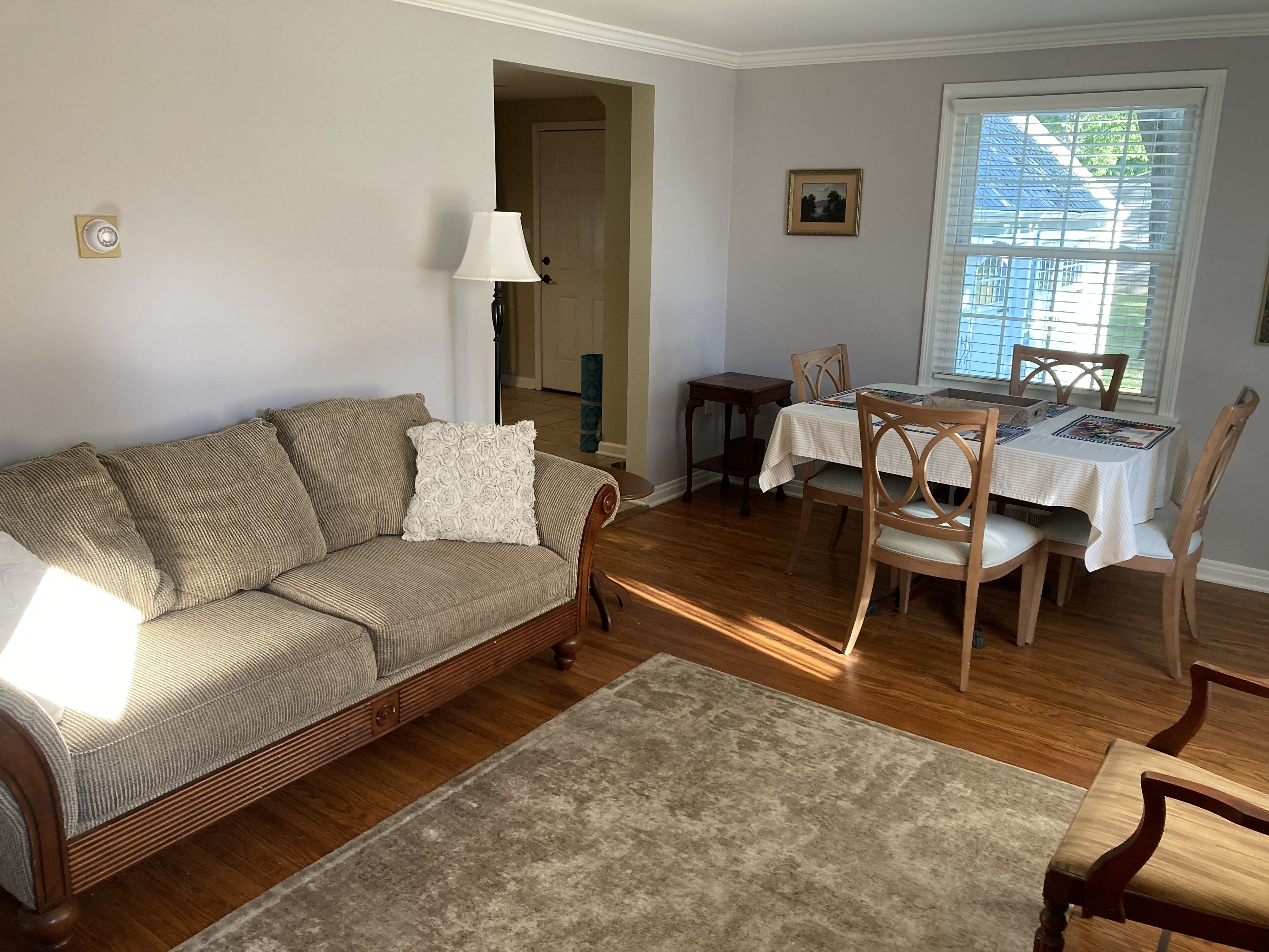 Un salon comprenant un canapé, une table à manger avec des chaises, une lampe et une fenêtre avec des stores.