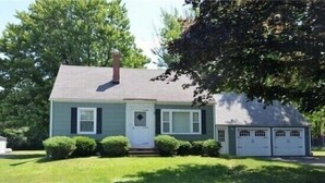 A single-story house with a front porch, a garage with two doors, and a chimney. - Buffalo Ny Carols Cape (Bowmansville)