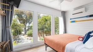 Ett sovrum med en säng, stora fönster, en takfläkt och utsikt över omgivningen.
