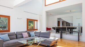 Ett modernt vardagsrum med en grå soffa, ett soffbord i glas och en matplats med ett piano.