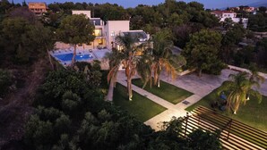 Ett modernt hus med en swimmingpool, omgivet av frodig grönska och palmer.