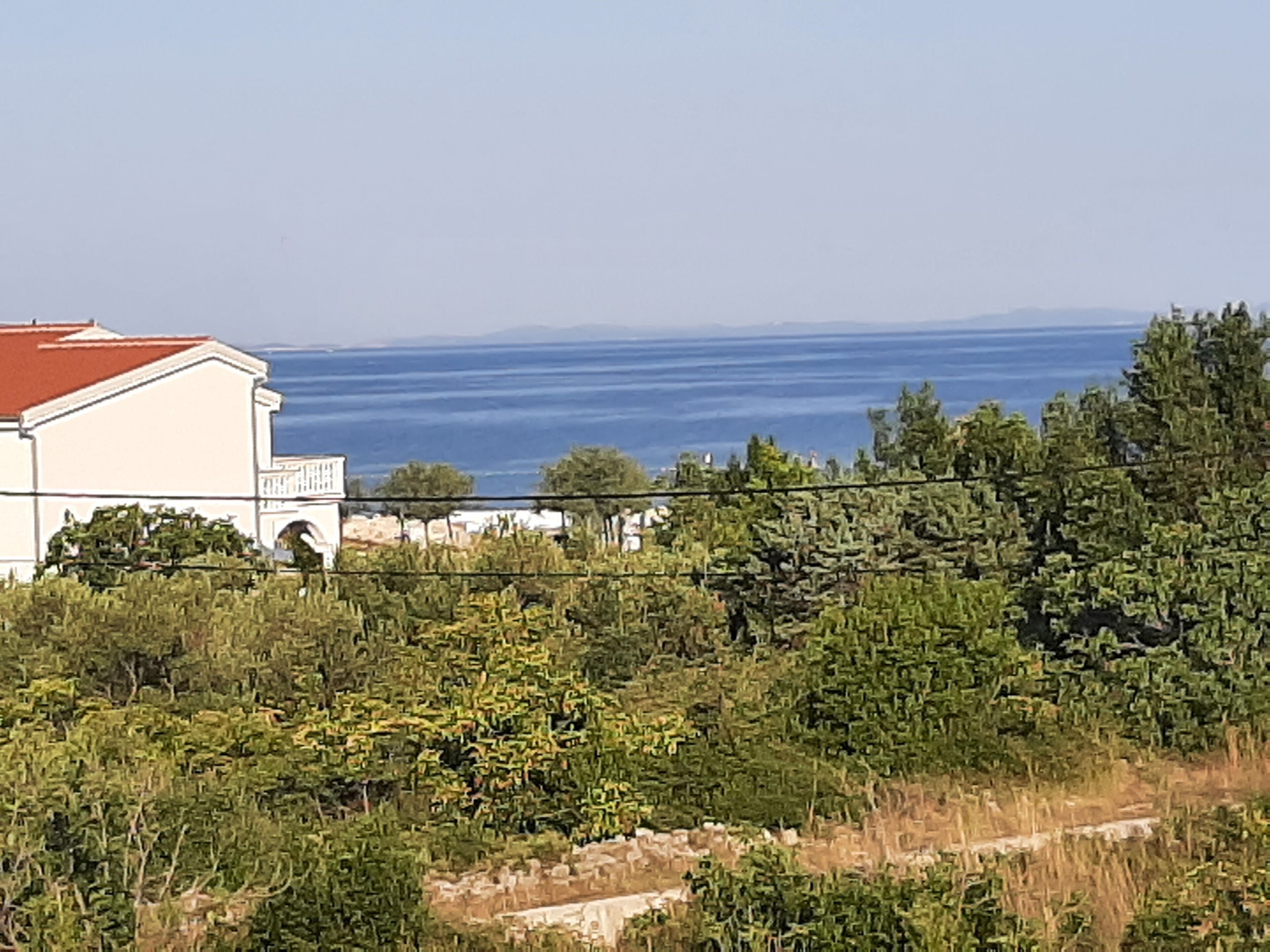A coastal building with a red roof, surrounded by dense greenery and a clear view of the sea.