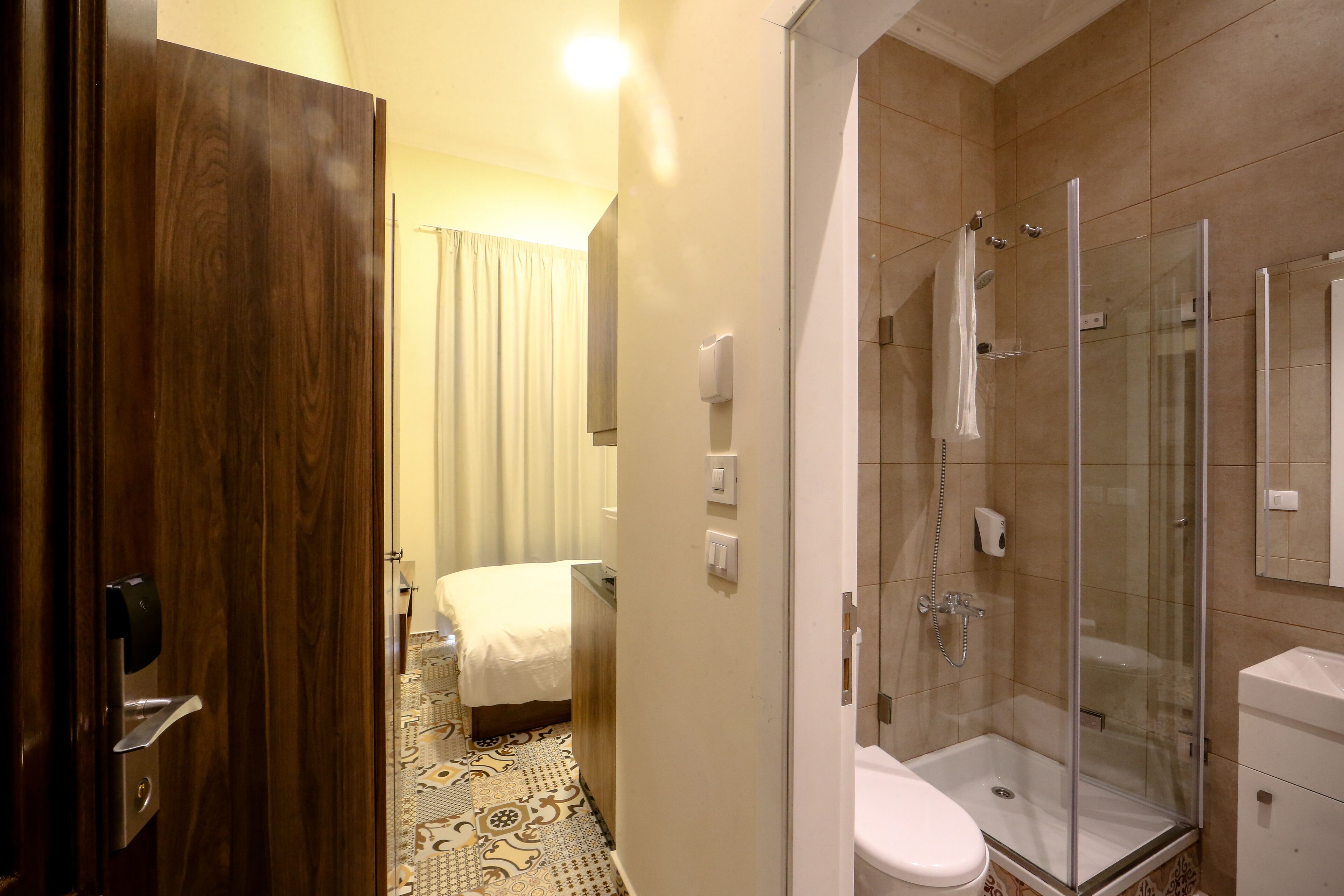 A hotel bathroom with a shower, toilet, and a bed with a patterned floor.