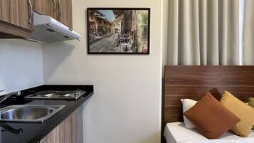 Ein kleines Hotelzimmer mit Küchenzeile, einem Bett mit Kissen, einem gemusterten Boden und einem gerahmten Bild an der Wand.
