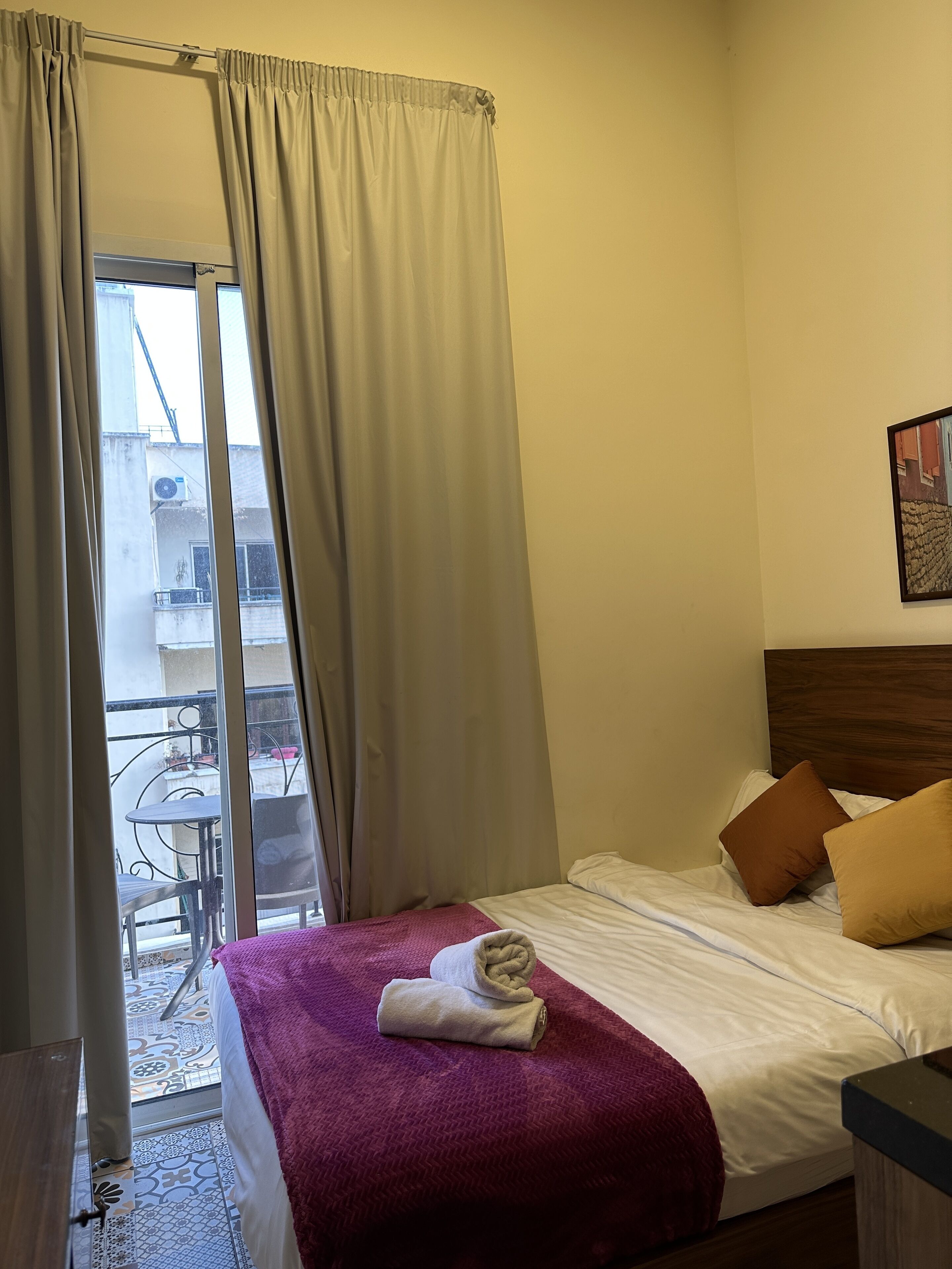 Habitación de hotel con cama, ventana con cortinas y vistas al balcón exterior, además de un cabecero de madera.