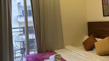 Habitación de hotel con cama, ventana con cortinas y vistas al balcón exterior, además de un cabecero de madera.