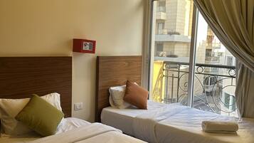 A hotel room with two beds, a wooden headboard, a window with curtains, and a view of buildings outside.