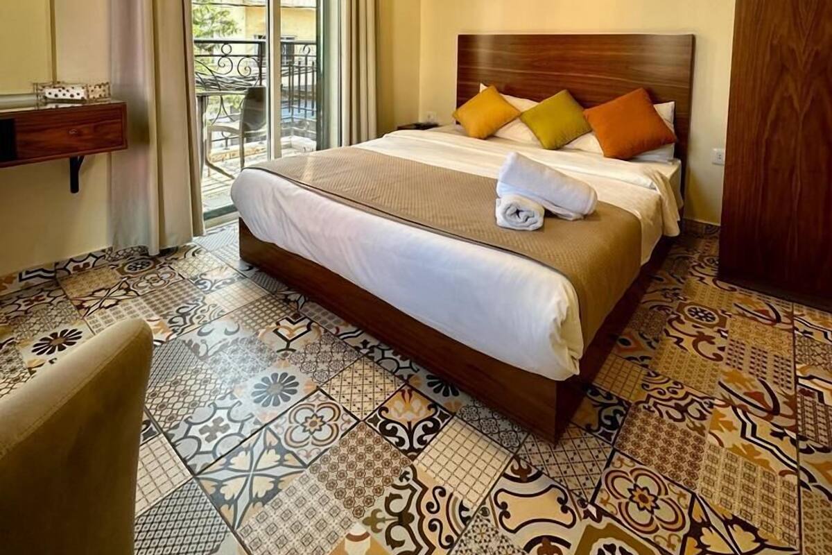 A hotel room with a large bed, a wooden headboard, a small desk, and a view of the outside balcony.