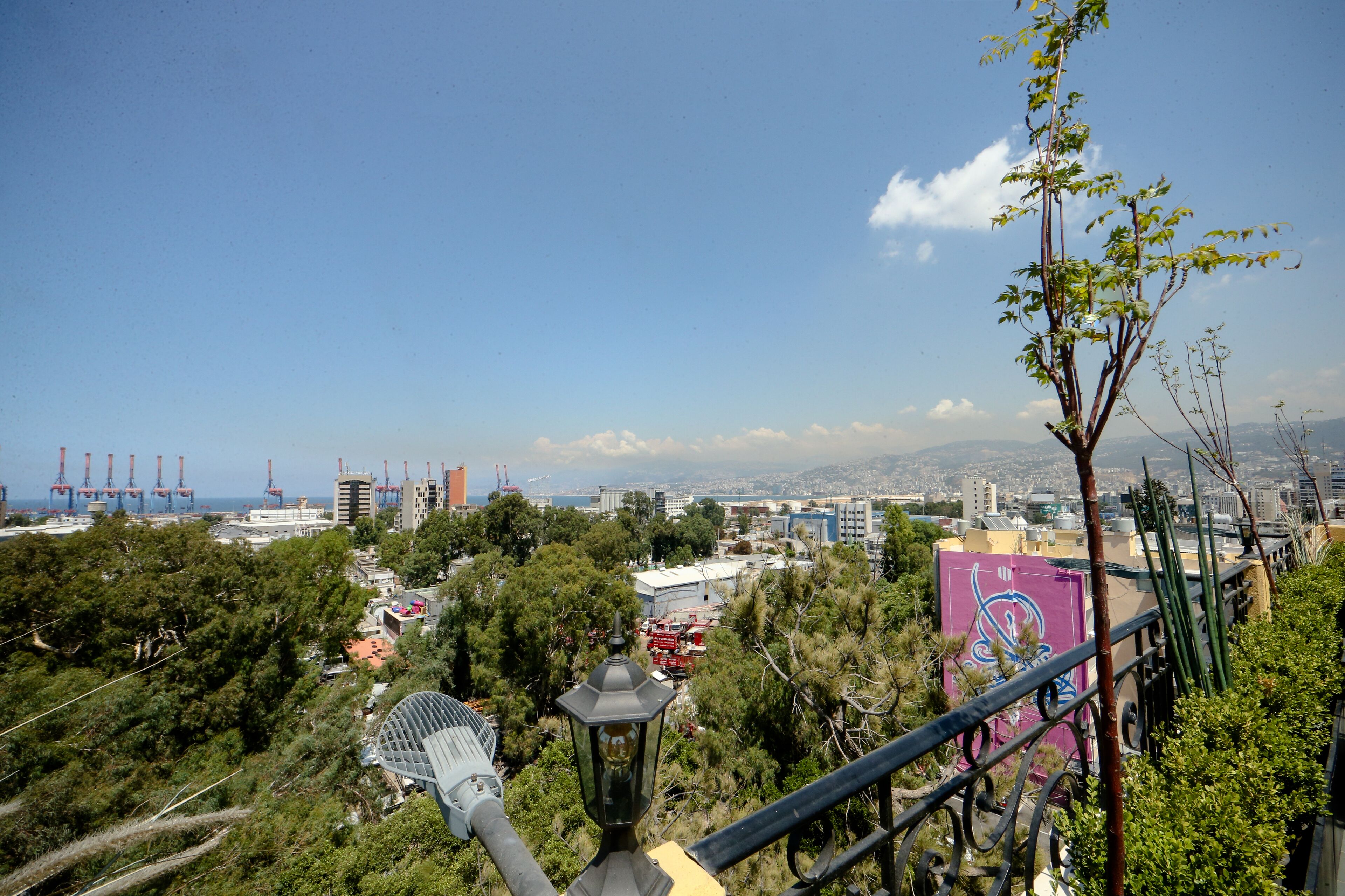 A high vantage point overlooking a cityscape with buildings, trees, and a clear sky.