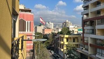 Un edificio de varios pisos con balcones y vistas a una calle con coches estacionados y una bandera.