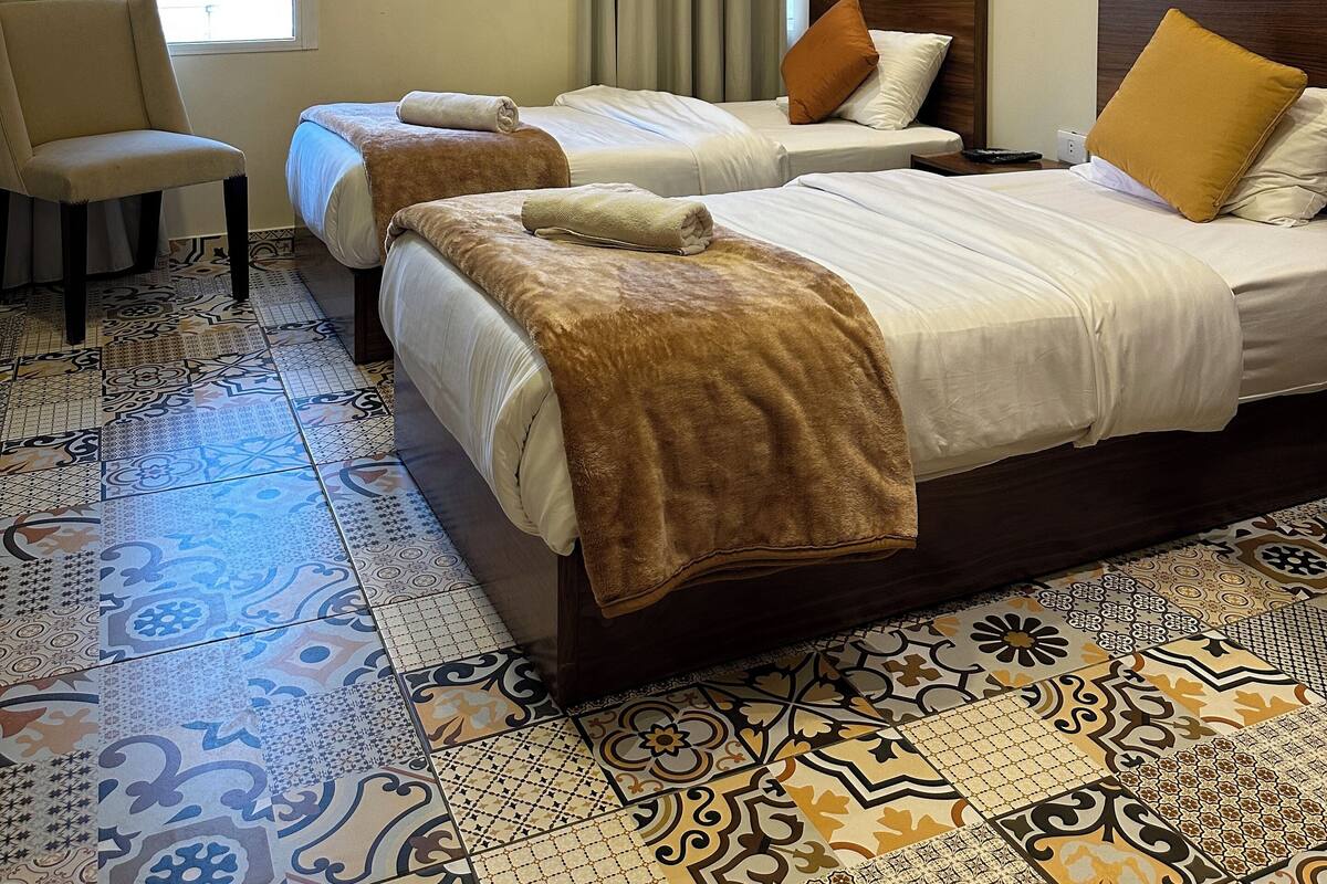 A hotel room with two beds, a chair, a painting, and patterned floor tiles.
