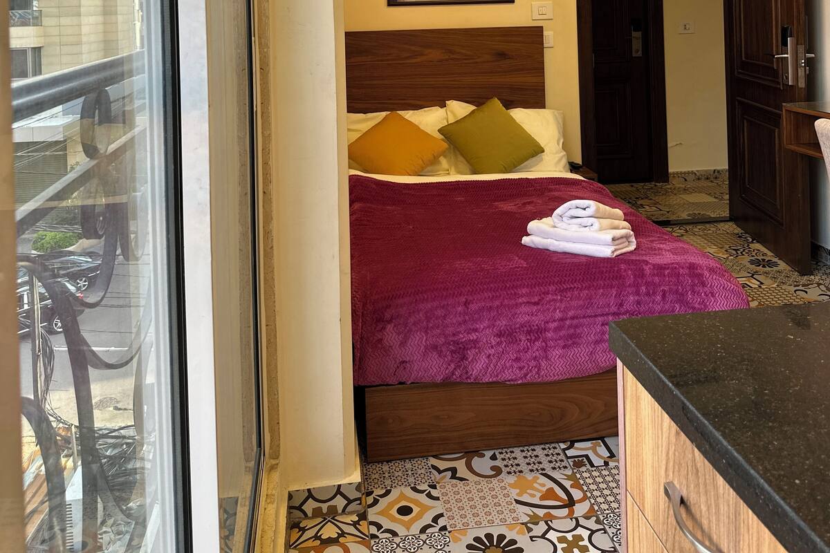 A hotel room with a bed, a window, a wall-mounted air conditioner, and a patterned floor.