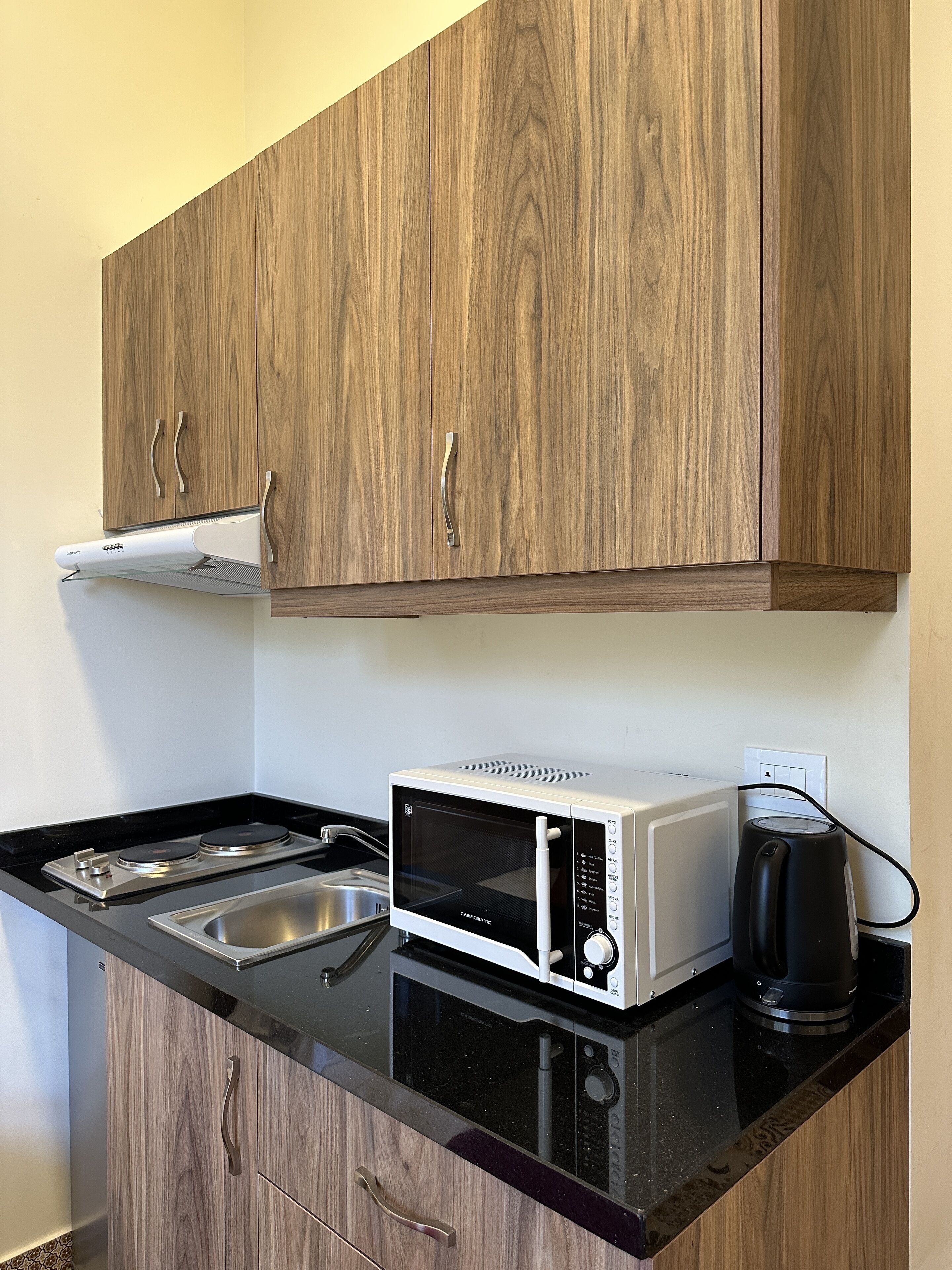 A compact kitchenette with a microwave, stove, sink, and wooden cabinets.