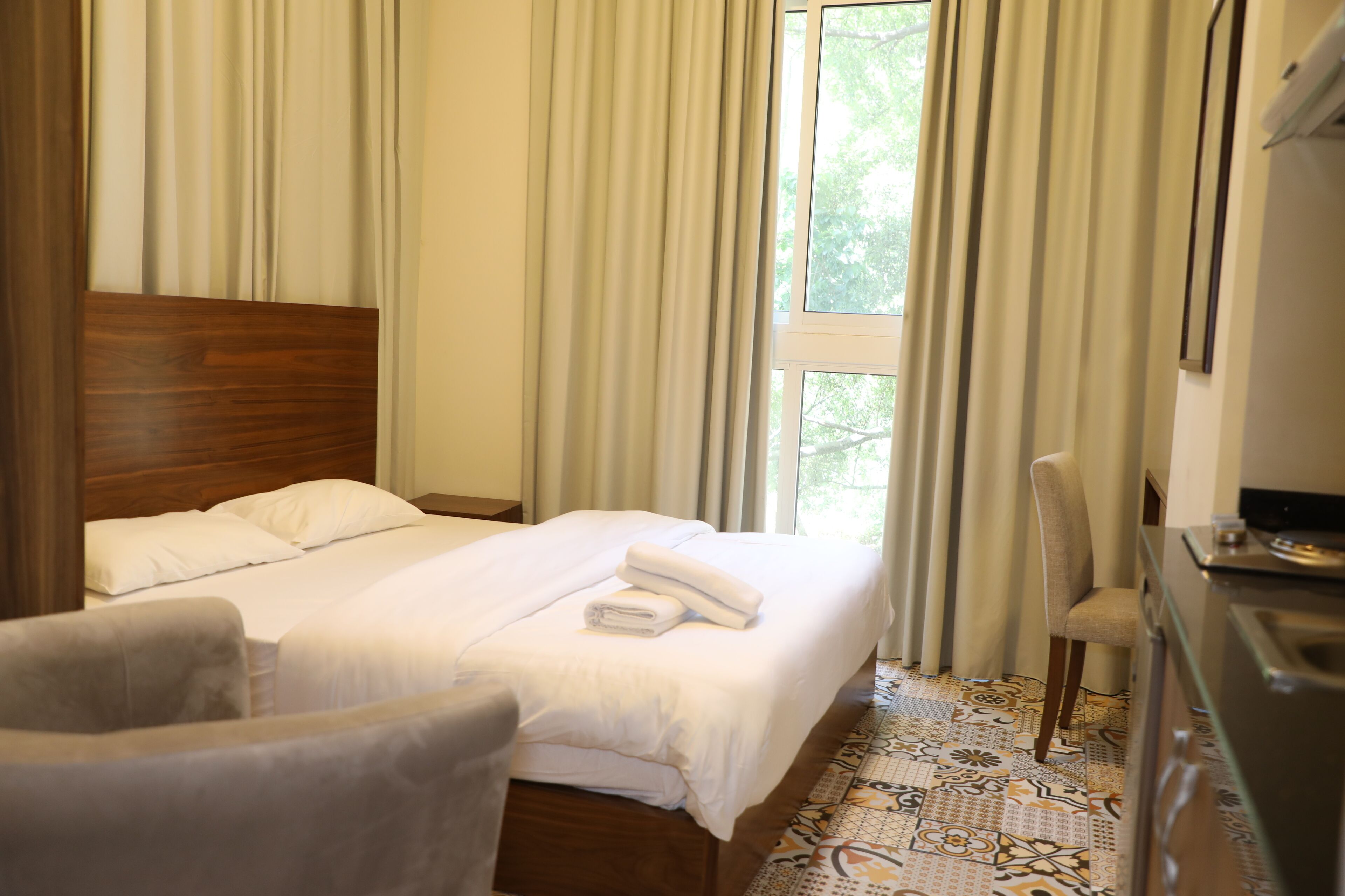 A hotel room with a bed, a chair, a desk, and a window with curtains.